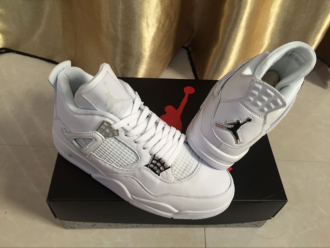 Pair of white Jordan 4 sneakers displayed on a black shoebox, showing the front, side mesh panels, laces, and tongue branding.