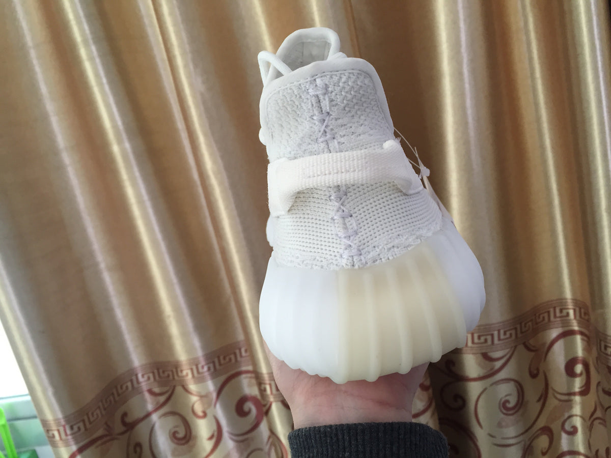 Rear close-up of a white sneaker showing the heel pull tab and ribbed sole unit.