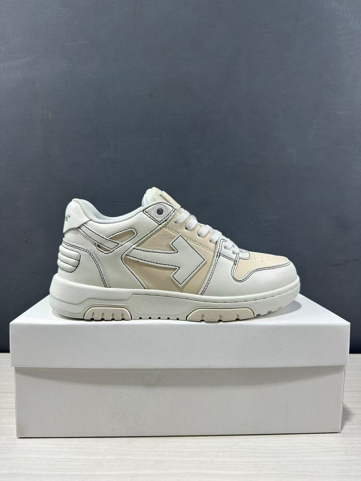 Side profile of a cream-white Off-White low-top sneaker displayed on a white box.