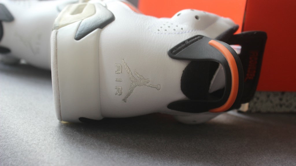 Close-up of the heel showing the white upper, black pull tab, orange accent, and embroidered Jumpman detail.