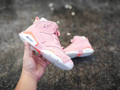 A hand holds one pink Air Jordan 6 sneaker while the matching shoe rests in the background.