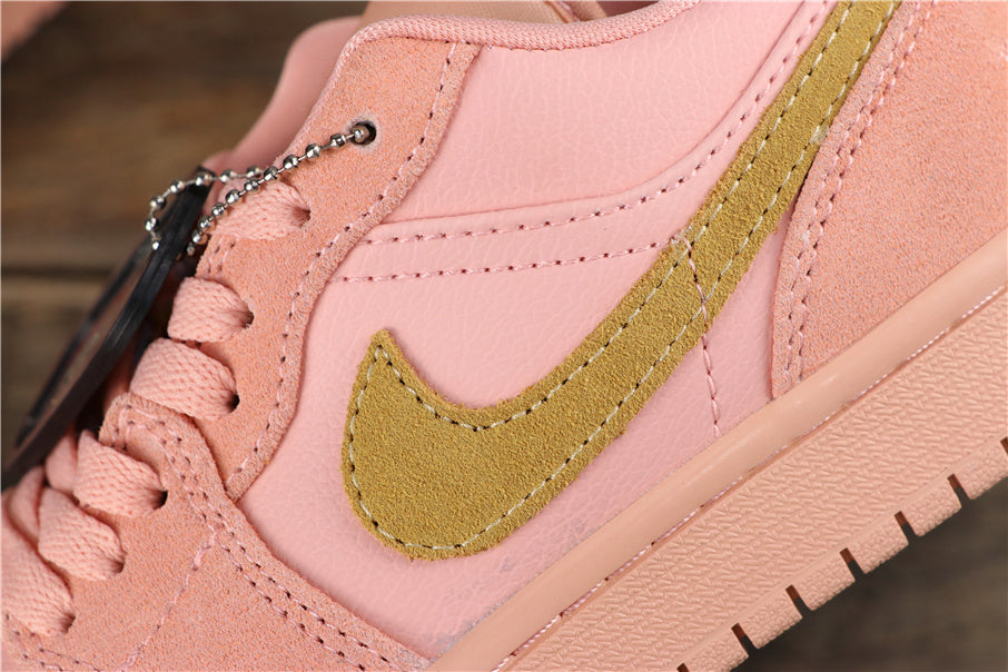 Close-up of the coral pink sneaker side showing the gold-toned swoosh-style side emblem, stitching, laces, and textured midsole.