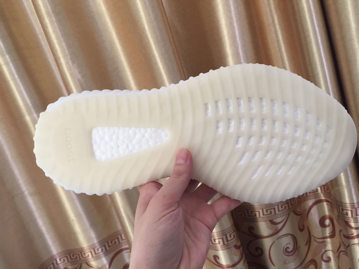 Underside view of one white sneaker showing the textured sole pattern and central inset.