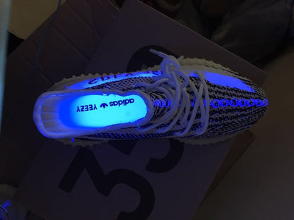 Top-down view of one sneaker under blue light with visible adidas YEEZY insole text.