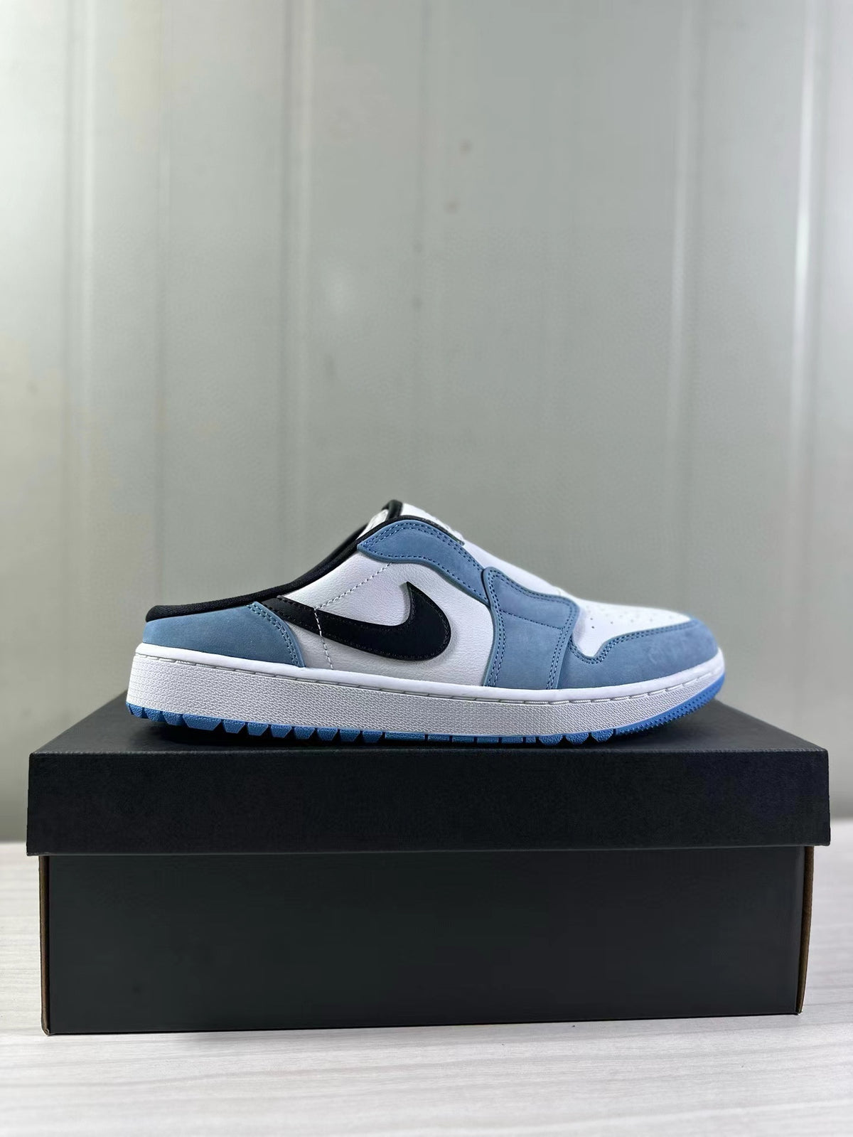 Side profile of the blue and white low-profile mule sneaker on a black box.