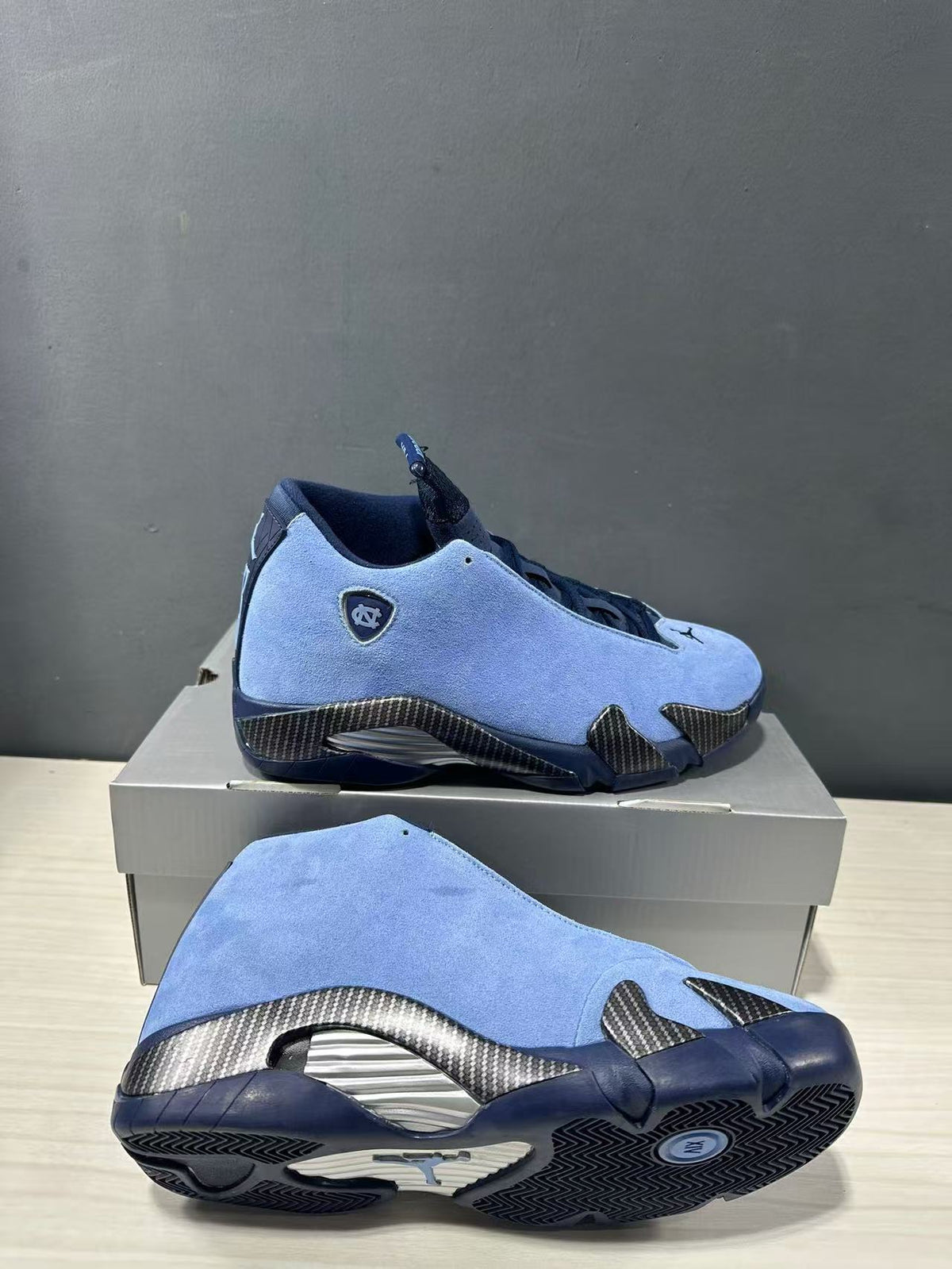 Blue and navy Jordan Air Jordan 14 sneakers shown from the side and outsole, highlighting textured panels and patterned tread.