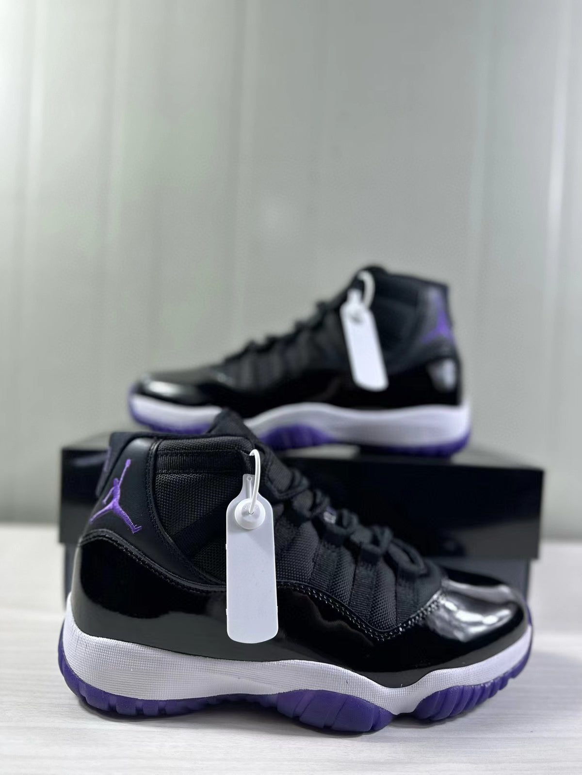 Angled view of the black and purple high-top sneaker pair with white hangtags.