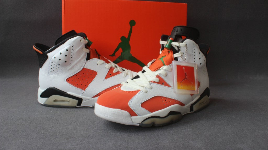 Pair of white, orange, and black high-top sneakers displayed in front of the orange shoe box.