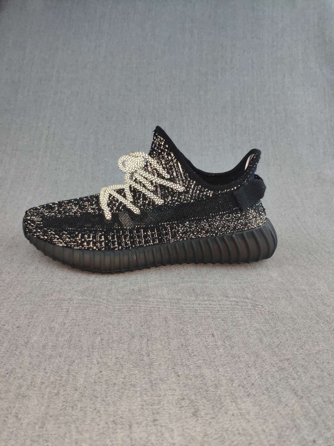 Side profile of a black 350 V2-style sneaker with a ribbed outsole, textured upper, and light-colored laces.