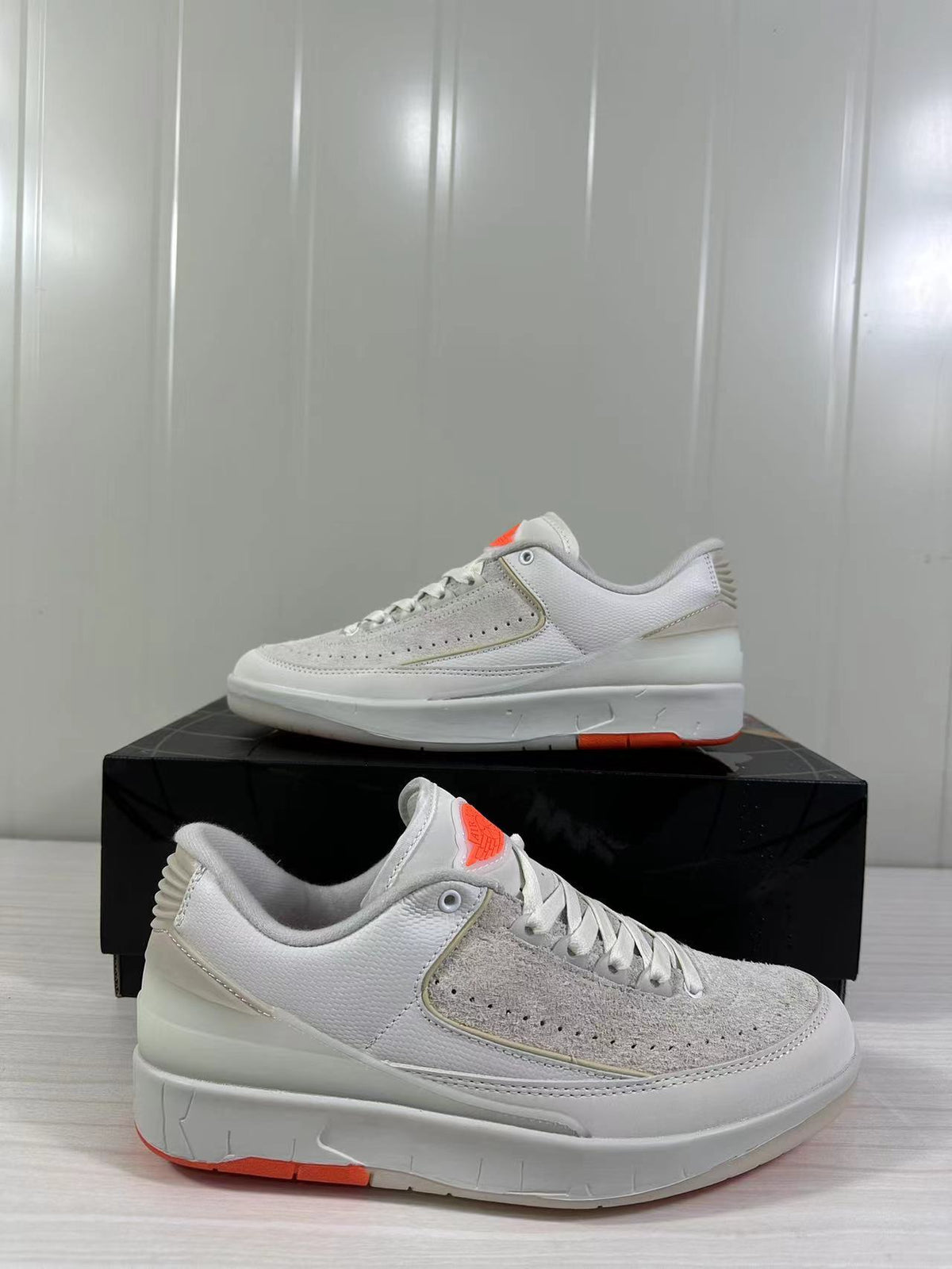 Close side view highlighting the perforated beige forefoot panel, white upper, sculpted midsole, and orange outsole.