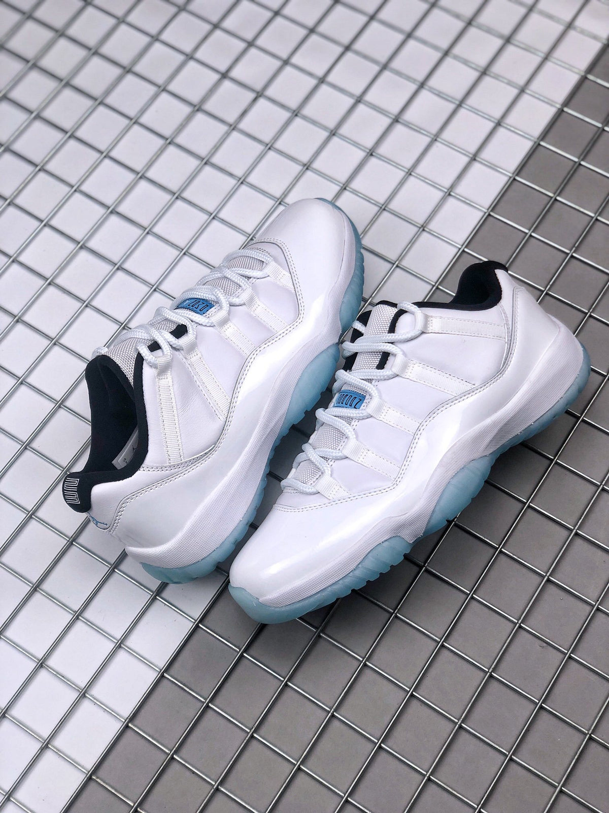 Pair of white Jordan Air Jordan 11 Low sneakers displayed on a metal grid surface.