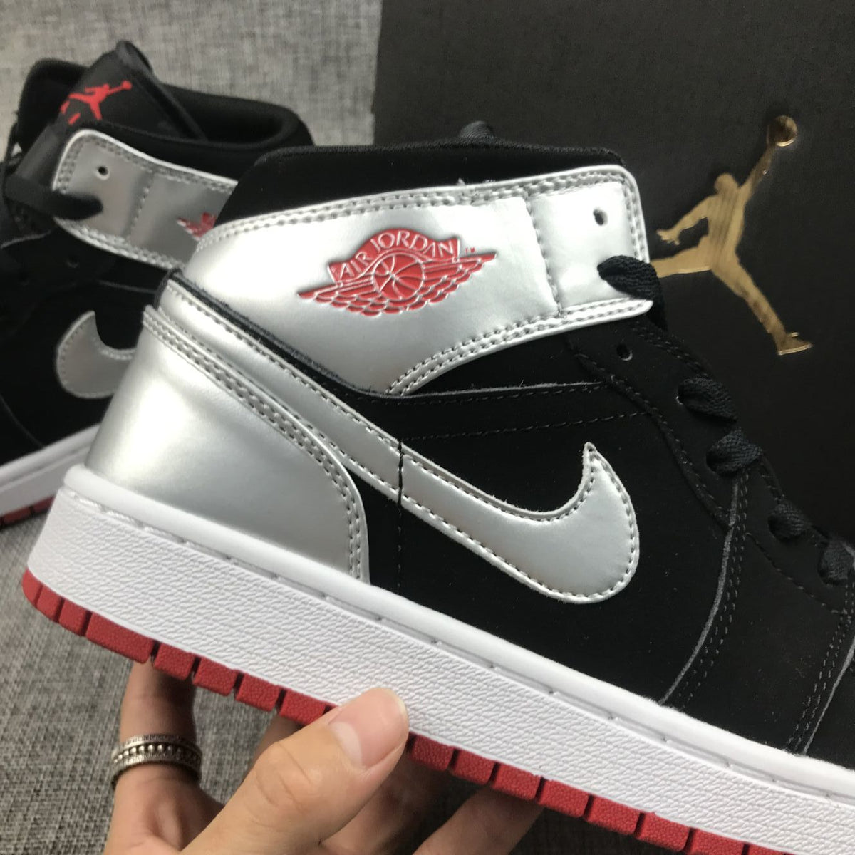 Close-up of the metallic silver collar and Swoosh on a black and silver Jordan mid-top sneaker.