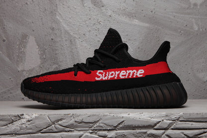 Side profile of the black sneaker with a red stripe, white Supreme lettering, and ribbed outsole.
