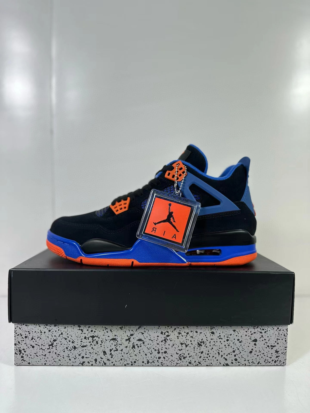 Side profile of the black, blue and orange Air Jordan 4 sneaker with attached hangtag.