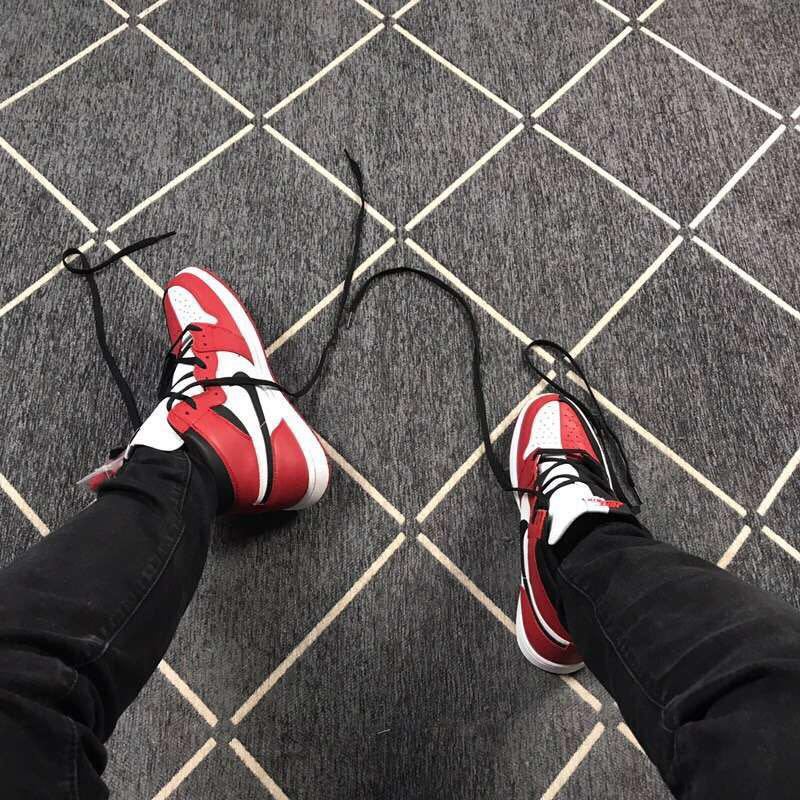The sneakers being worn, viewed from above, with black laces and red and white toe panels visible.