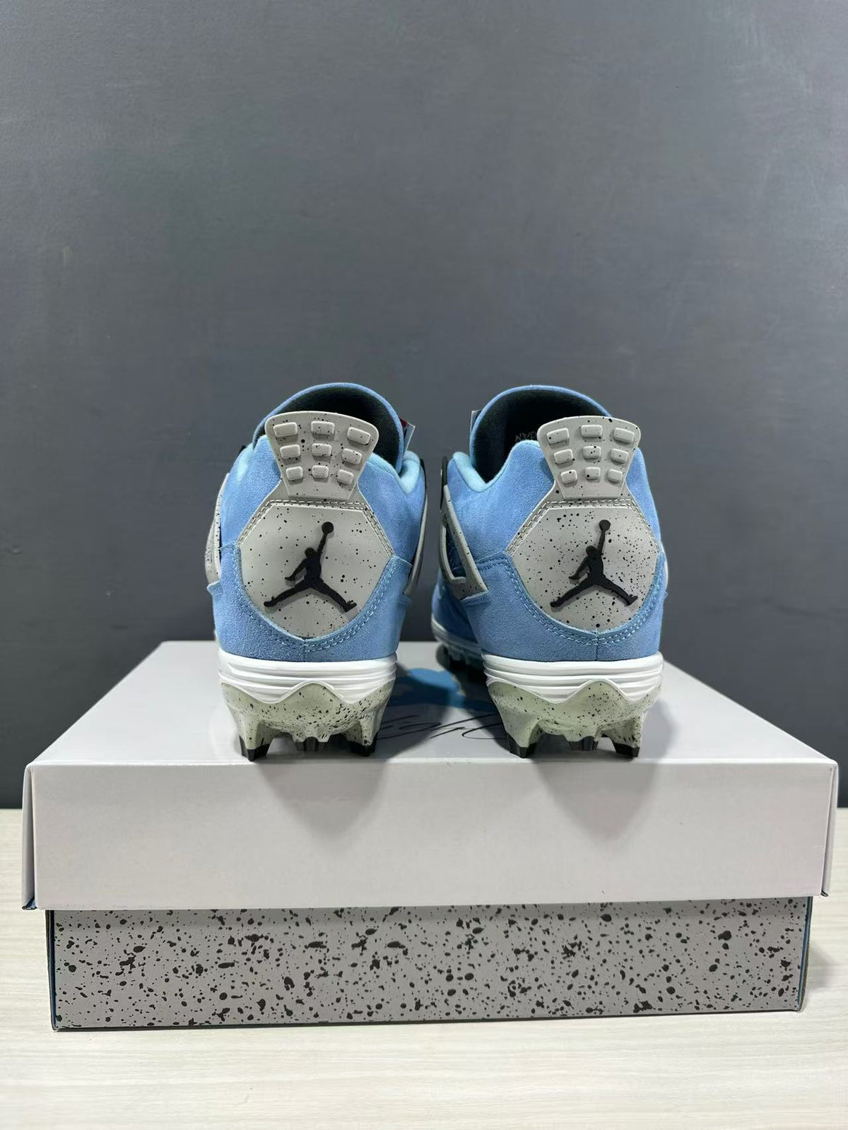 Rear view of the paired University Blue Jordan Air Jordan 4 sneakers showing the heel branding and studded outsoles.