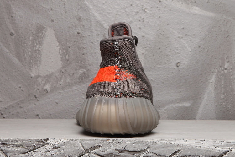 Rear view of the Yeezy 350 V2 sneaker showing the orange stripe, raised heel, and ribbed translucent sole.