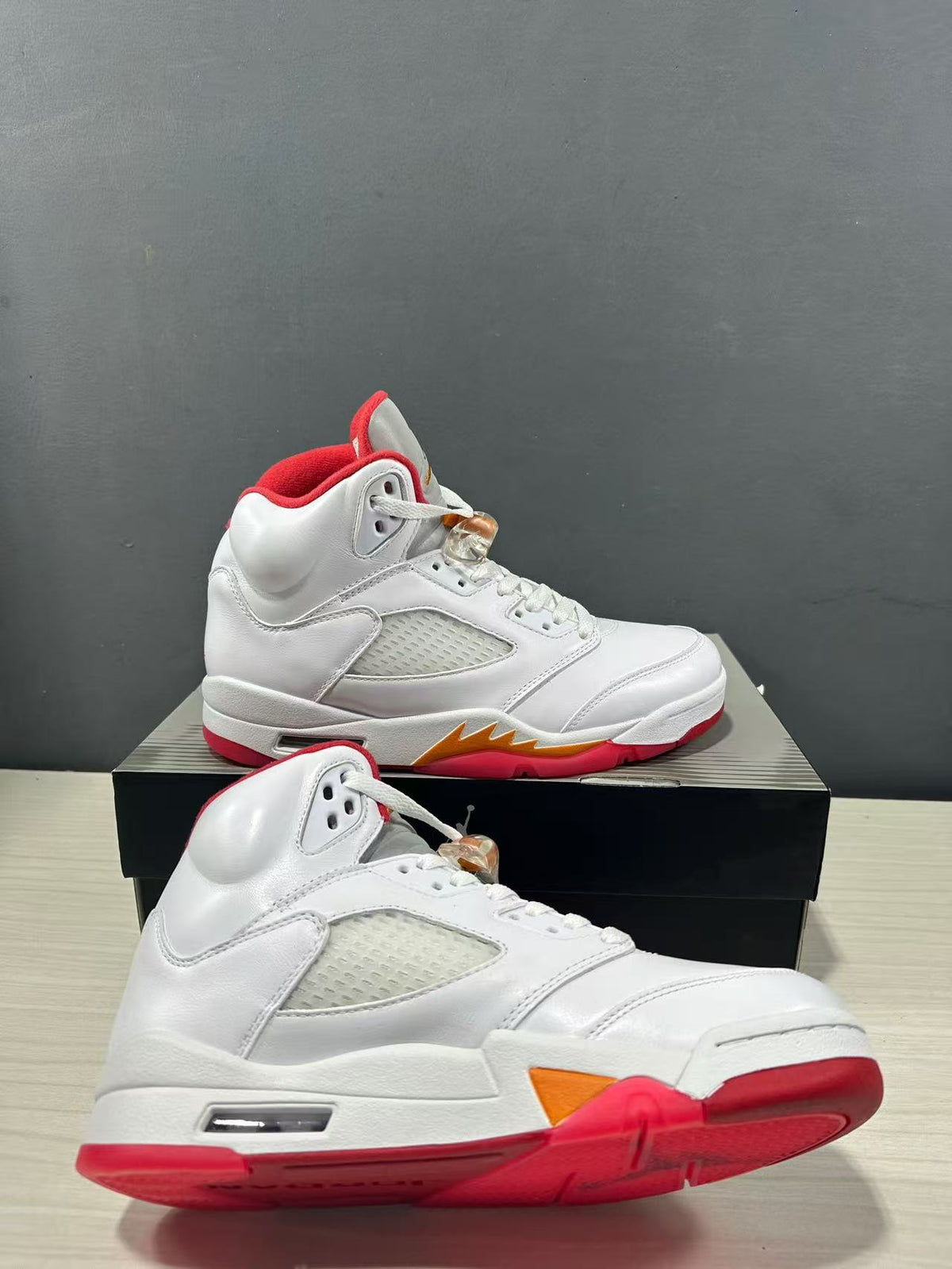 Two white high-top sneakers shown from angled side and outsole views, featuring red soles and orange midsole detailing.