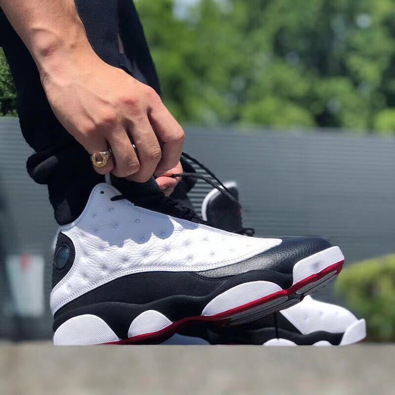 Close side view showing the white textured upper, black overlays, circular side detail, and red outsole accent.
