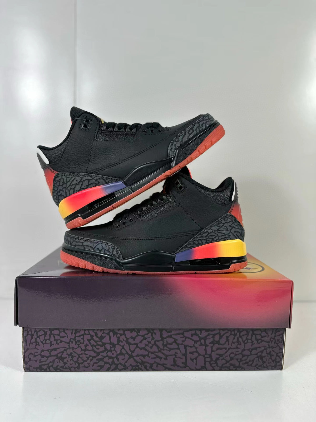 Side profile of the black mid-top sneakers displayed on the shoebox, highlighting the patterned overlays and multicolor midsole.