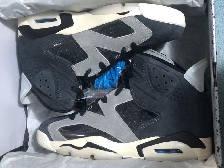 Pair of black and grey high-top Jordan sneakers resting inside an open shoebox, with spare blue laces visible.