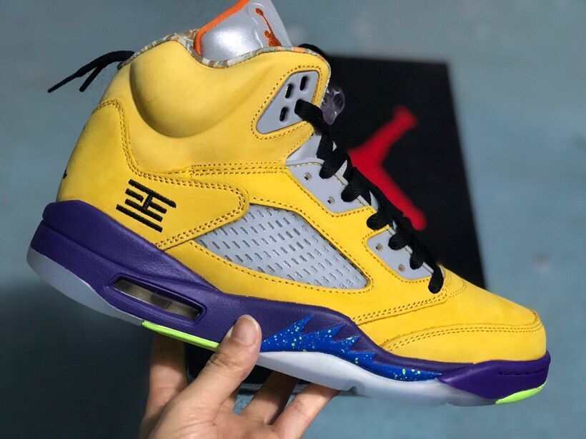 Angled side view of the yellow high-top sneaker showing black laces, mesh panel, purple midsole, and patterned outsole details.