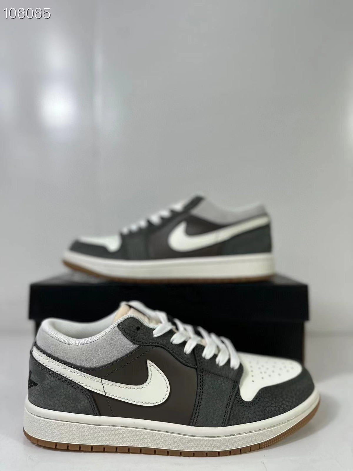 Pair of black, white and grey low-top sneakers shown from a side angle on a black shoe box.