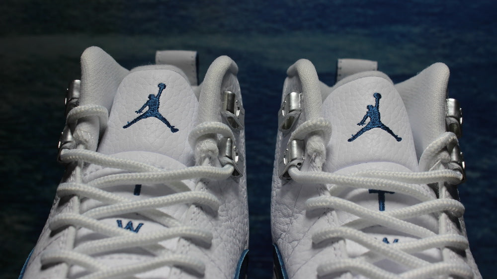 Front close-up of both tongues with navy Jordan logos and white laces.