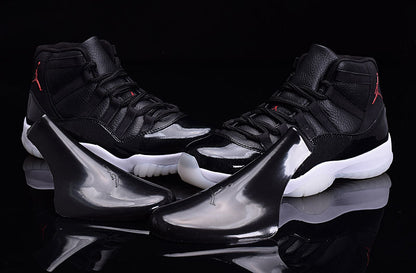 Pair of black and white high-top Jordan sneakers with red branding, displayed with glossy black shoe accessories.
