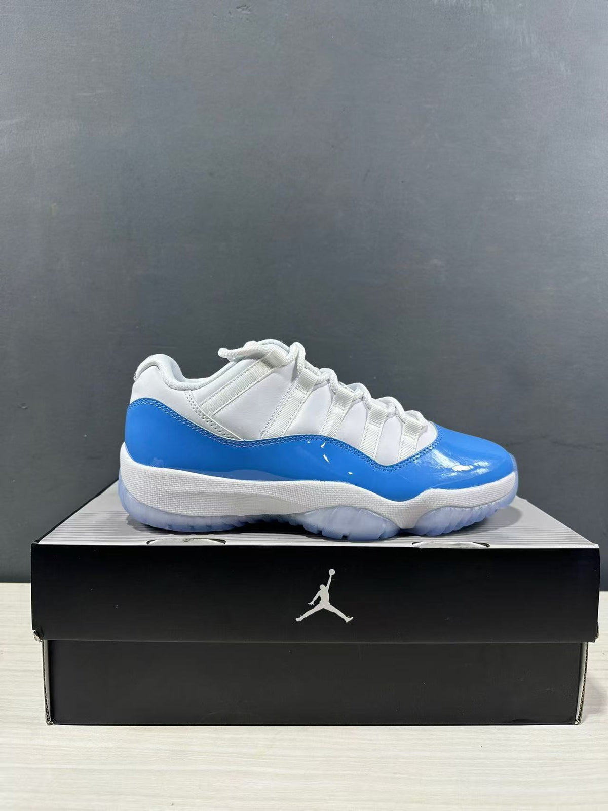 Side profile of a white and university blue low-top sneaker displayed on a black shoe box.