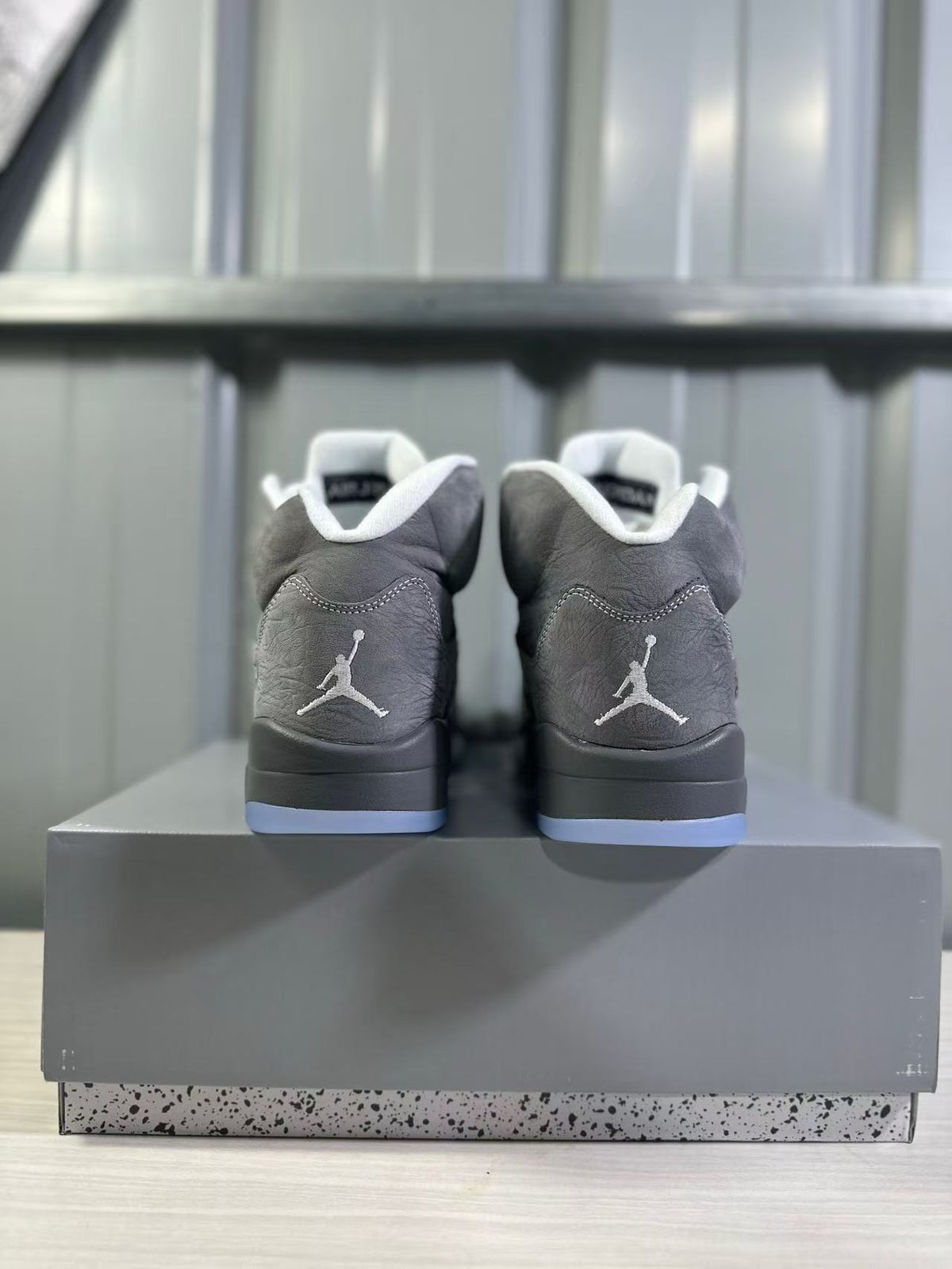 Rear view of grey high-top sneakers showing white heel logos, black midsoles, translucent blue outsoles, and a grey shoe box.