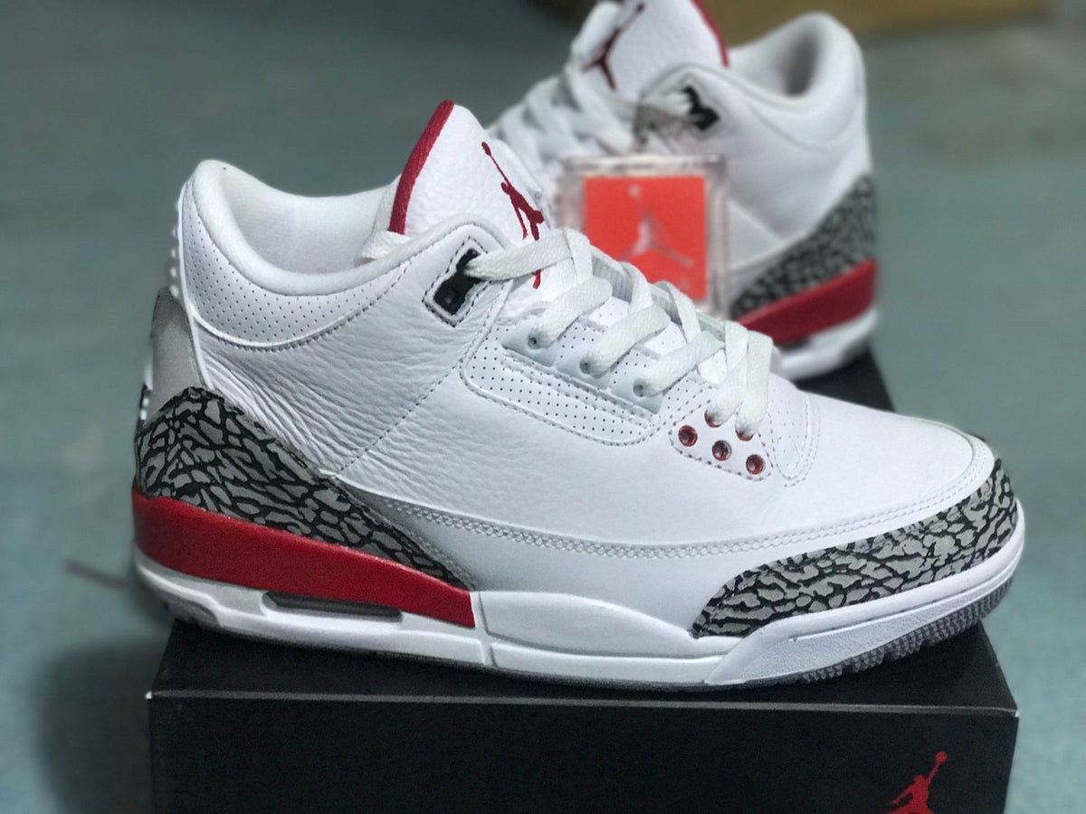 Side view of a white Jordan 3 Retro sneaker with elephant-print overlays and red heel detail
