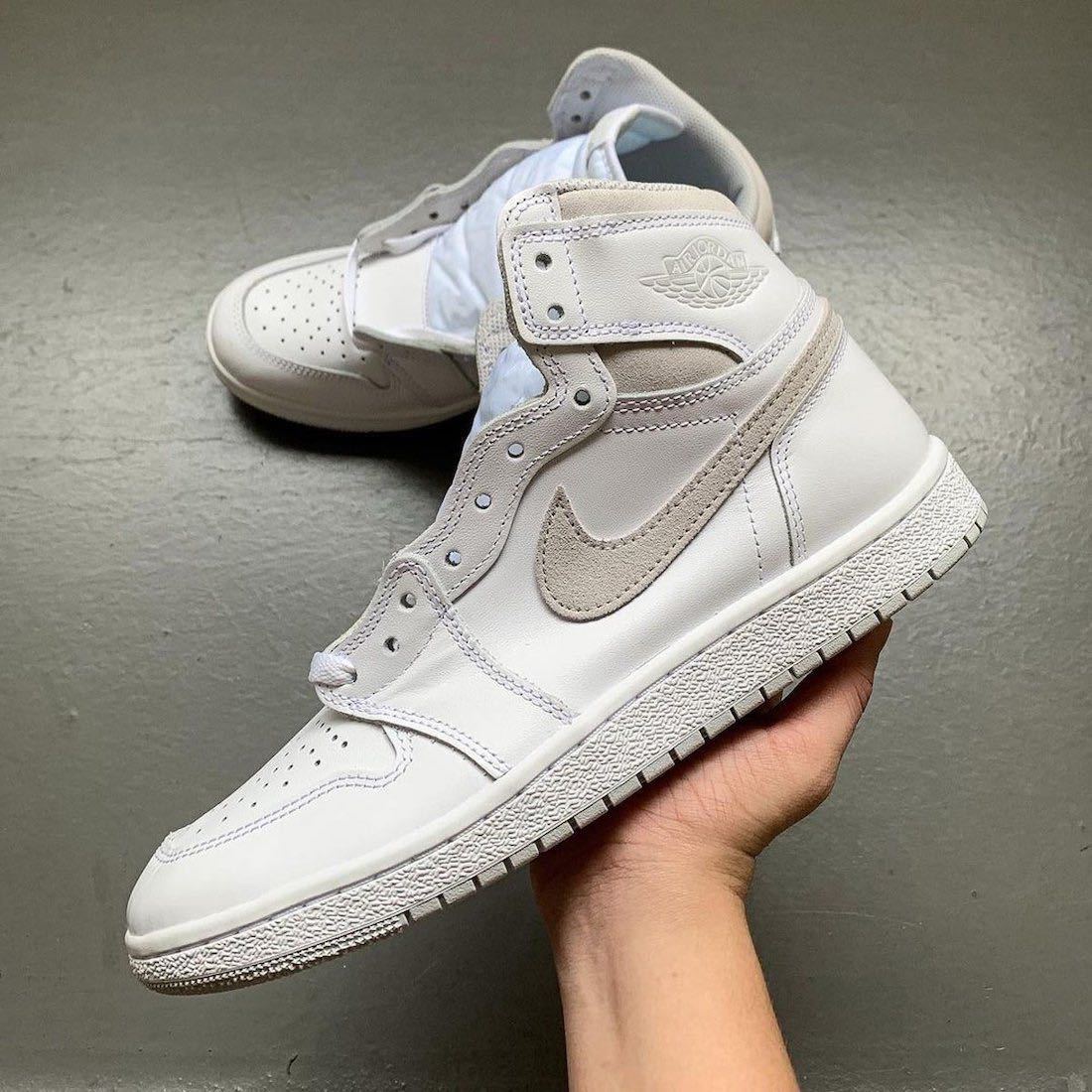 White and grey high-top sneaker shown in hand from the side with a second shoe in the background.