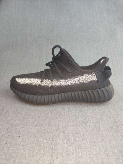 Side profile of a single black sneaker with a reflective stripe, padded collar, and thick ribbed outsole.