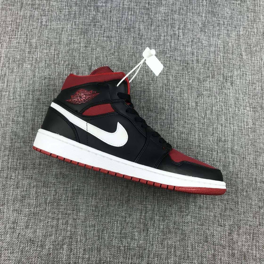 Side view of a black, red, and white Jordan Air Jordan 1 Mid sneaker on gray fabric.