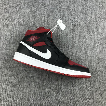 Side view of a black, red, and white Jordan Air Jordan 1 Mid sneaker on gray fabric.