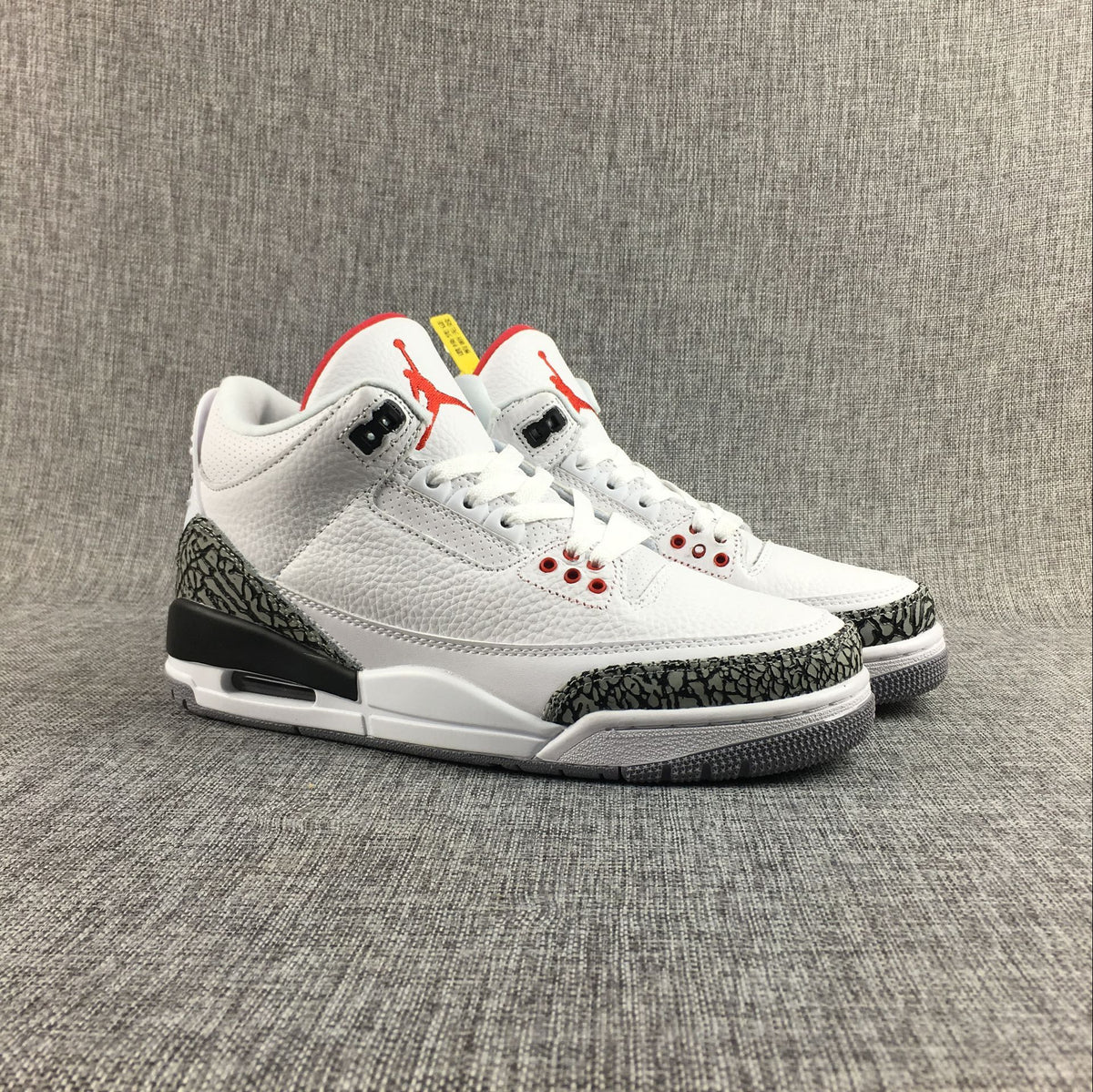 Pair of white Jordan 3 sneakers shown at an angle with red tongue accents and elephant-print overlays