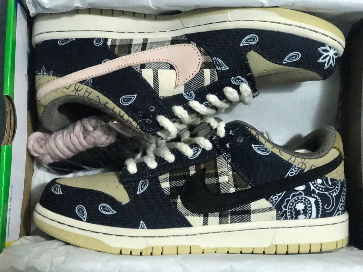Pair of low-top sneakers inside a colorful shoebox, showing black patterned uppers, plaid panels, light laces, and beige soles.