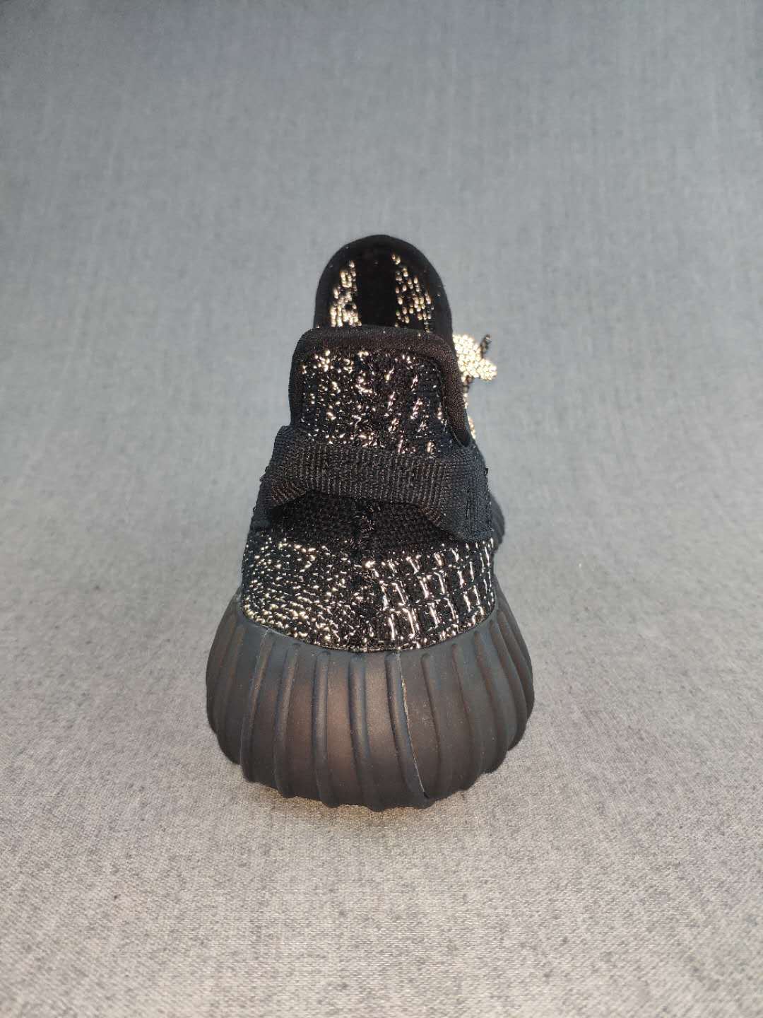 Rear view of a black sneaker showing the heel pull tab, textured upper, and ribbed dark outsole.