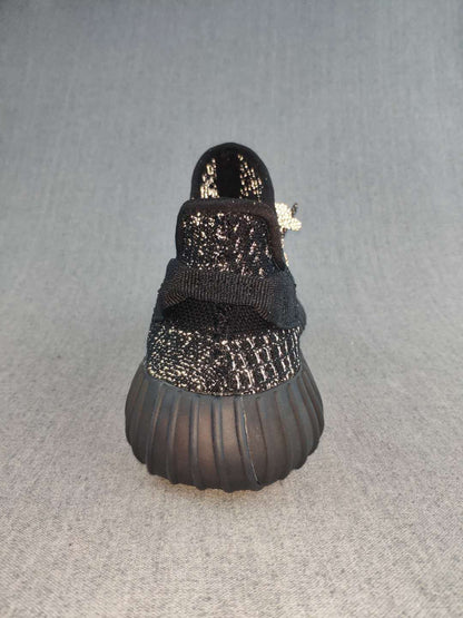 Rear view of a black sneaker showing the heel pull tab, textured upper, and ribbed dark outsole.