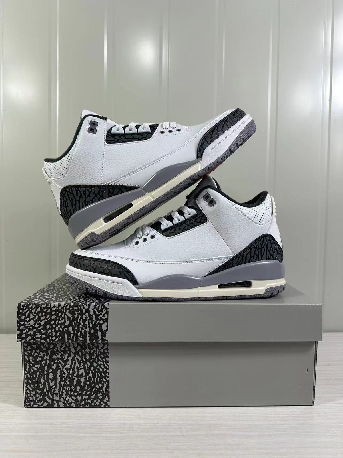 Lifestyle display of two white and grey Air Jordan 3 sneakers, one resting above the other.