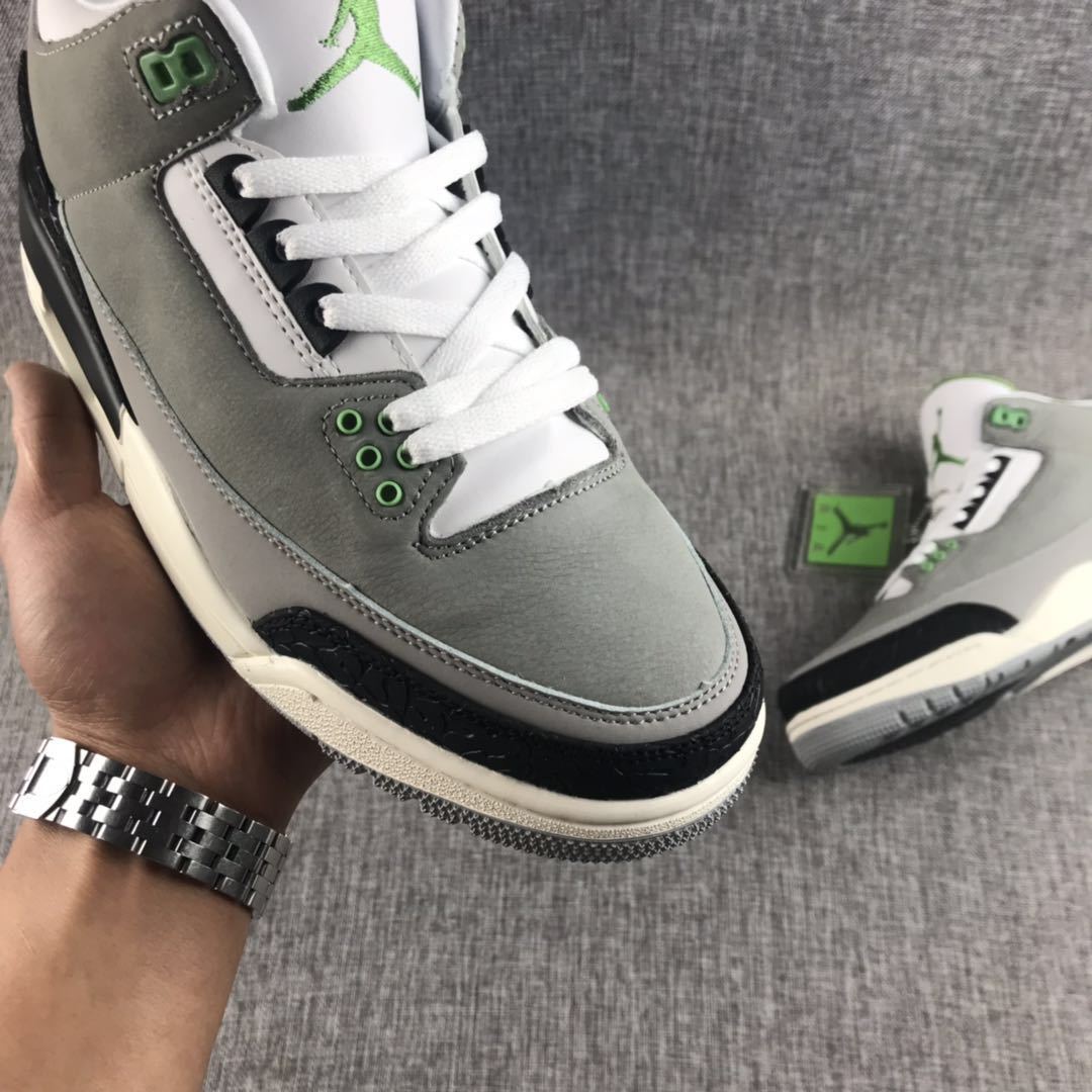 Close-up side view showing the gray upper, white laces, green eyelets, and black textured toe overlay.