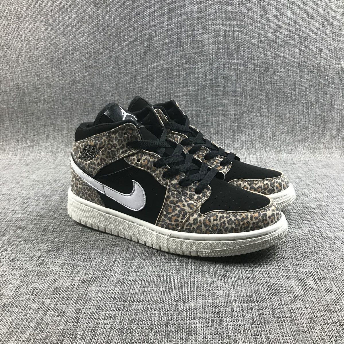Three-quarter front view of the pair with leopard-print overlays, black toe boxes, white Swooshes, and white outsoles.