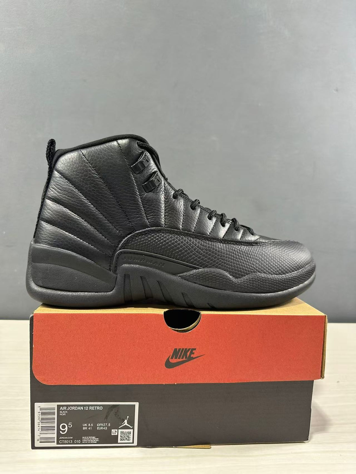 Black Jordan Air Jordan 12 high-top sneaker displayed on its shoebox; the box label shows EU 43, US Men 9.5, UK 8.5, and CM 27.5.