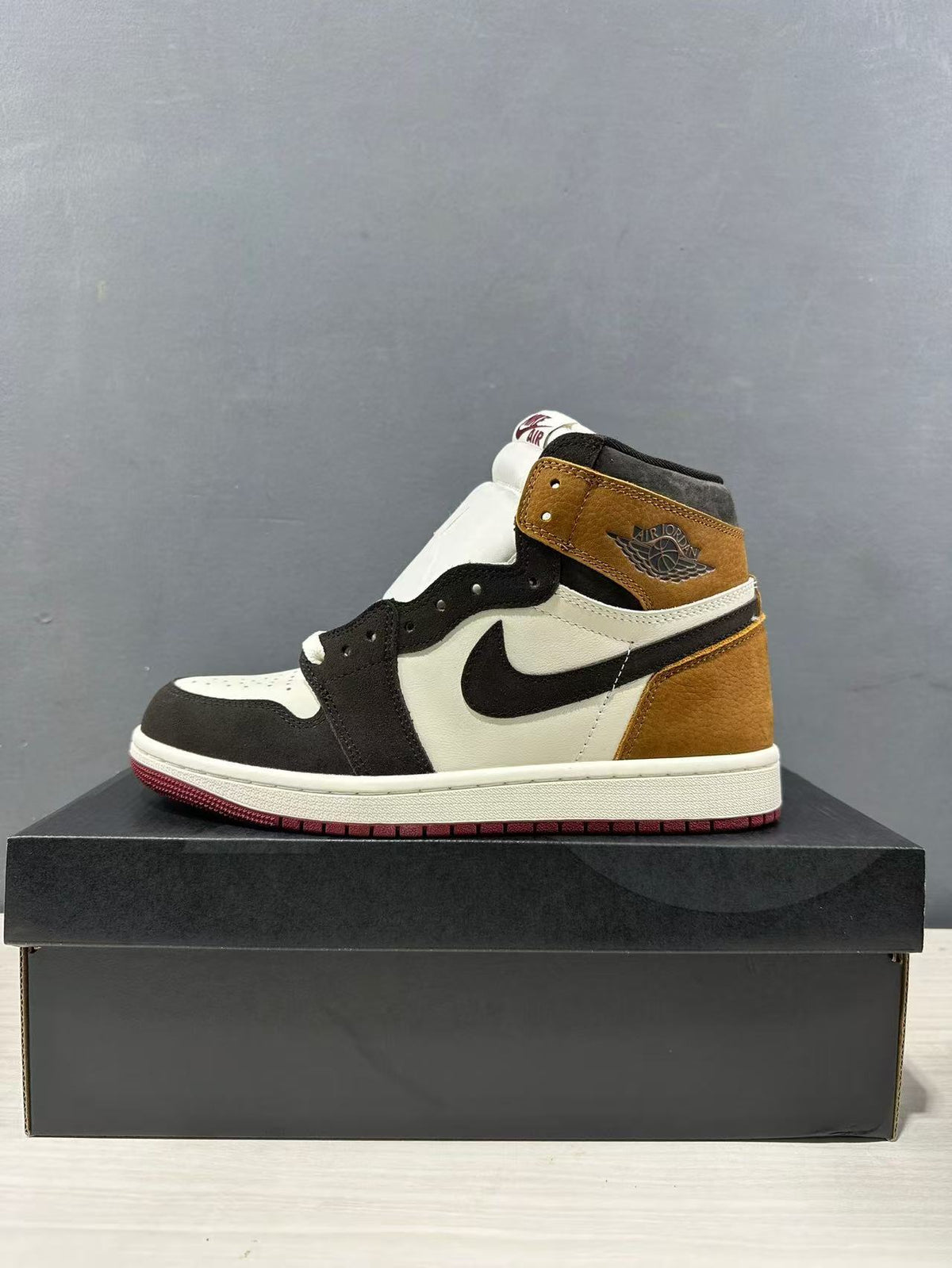 Side profile of the high-top sneaker with a brown collar and heel, black overlays, white midsole and burgundy outsole.