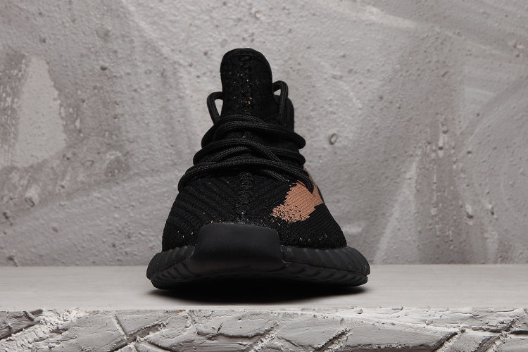 Front view of a black Yeezy 350 V2-style sneaker with black laces, textured upper, and a peach-toned side detail.