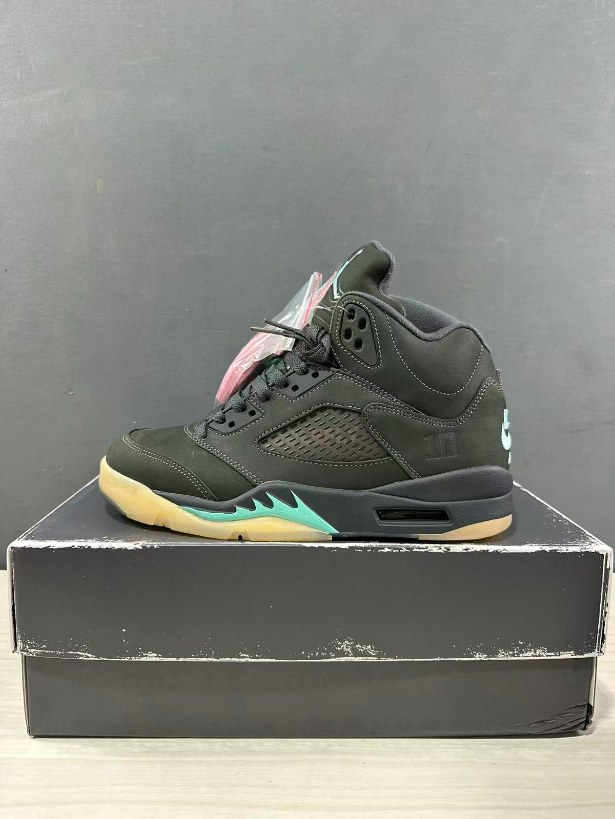 Side profile of a dark green Jordan Air Jordan 5 sneaker with perforated paneling, black midsole, and aqua accent detail.