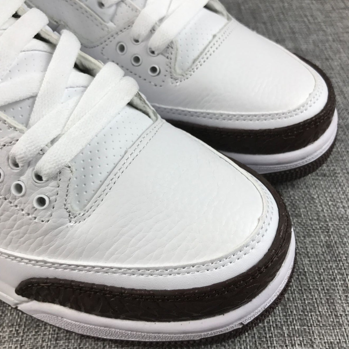 Close-up of the white toe area, perforated lace panel, stitching, and textured brown overlay.