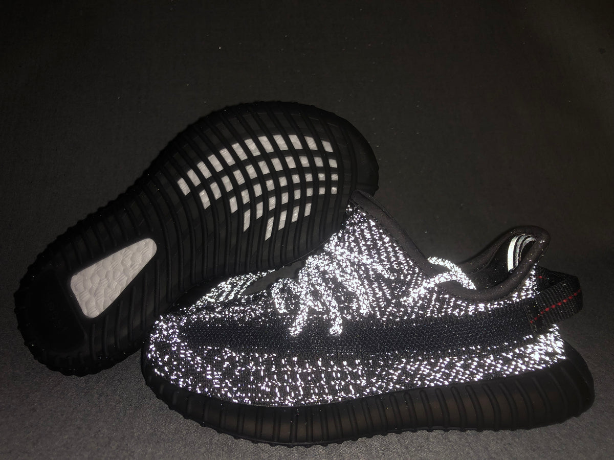 Flash-lit view highlighting the reflective detailing across the black sneaker upper.