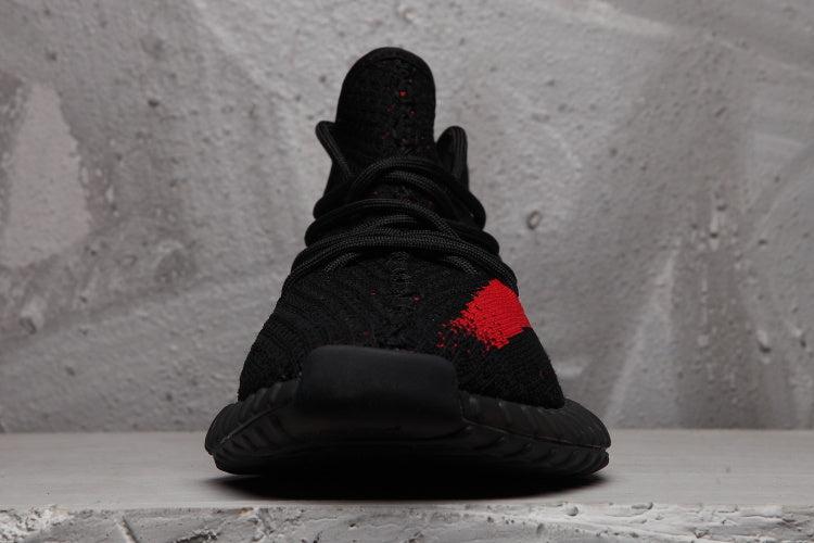 Front view of the black lace-up sneaker with a black toe, red side detail, and textured sole.